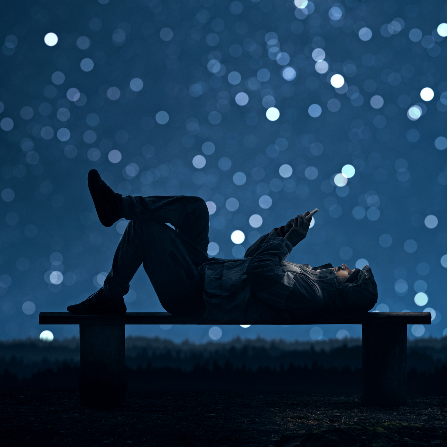 A man is lying on a bench and using a smartphone