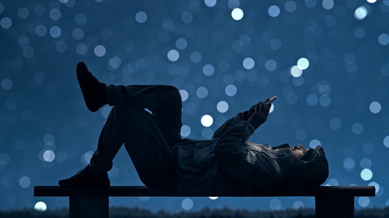 A man is lying on a bench and using a smartphone