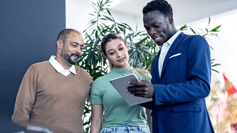 Car salesman using digital tablet talking about new car to customers in a store