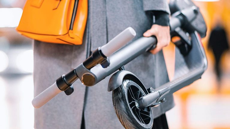 Modern businesswoman carrying an e-scooter while heading to work