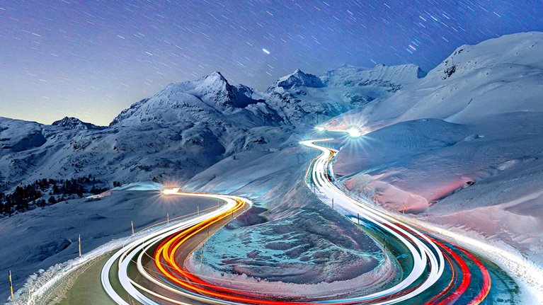 Car trail lights on snowy mountain road