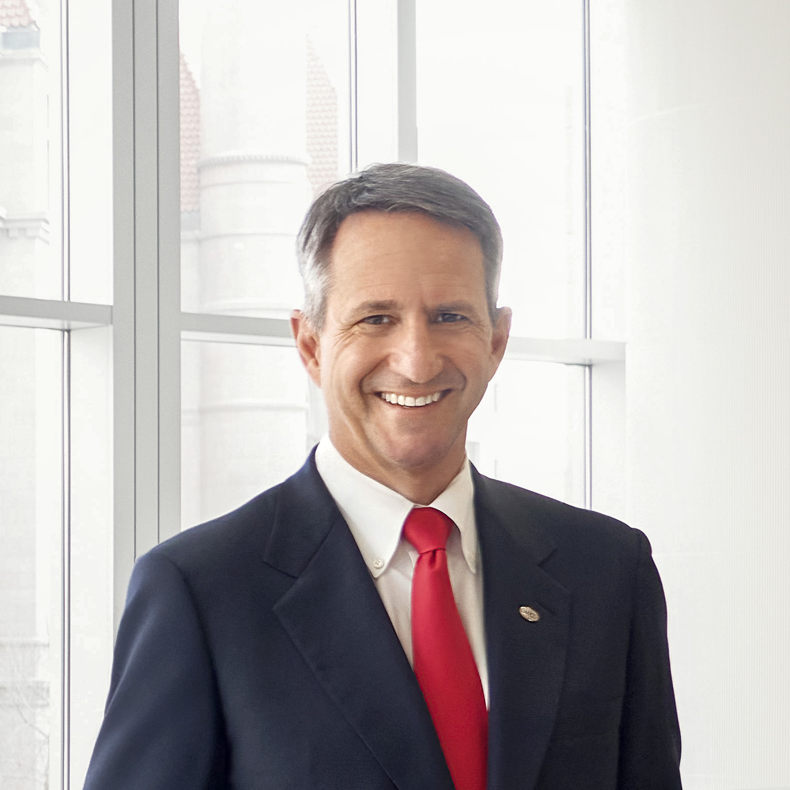 Wearing a dark blue suit, Christophe Beck, CEO of Ecolab, stands by a large window.