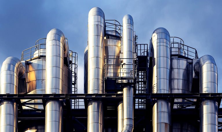 Image of interwoven chemical pipes at a factory shining in the sunset.