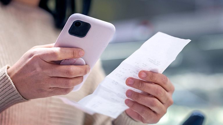 Young woman examining list while using smart phone at supermarket
