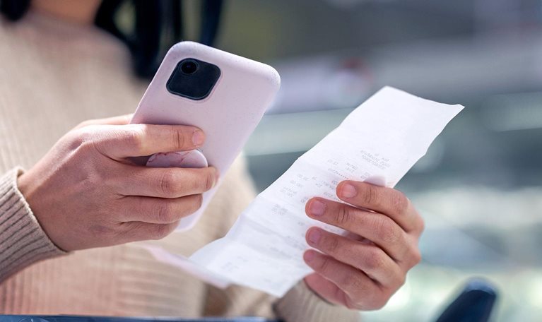 Young woman examining list while using smart phone at supermarket