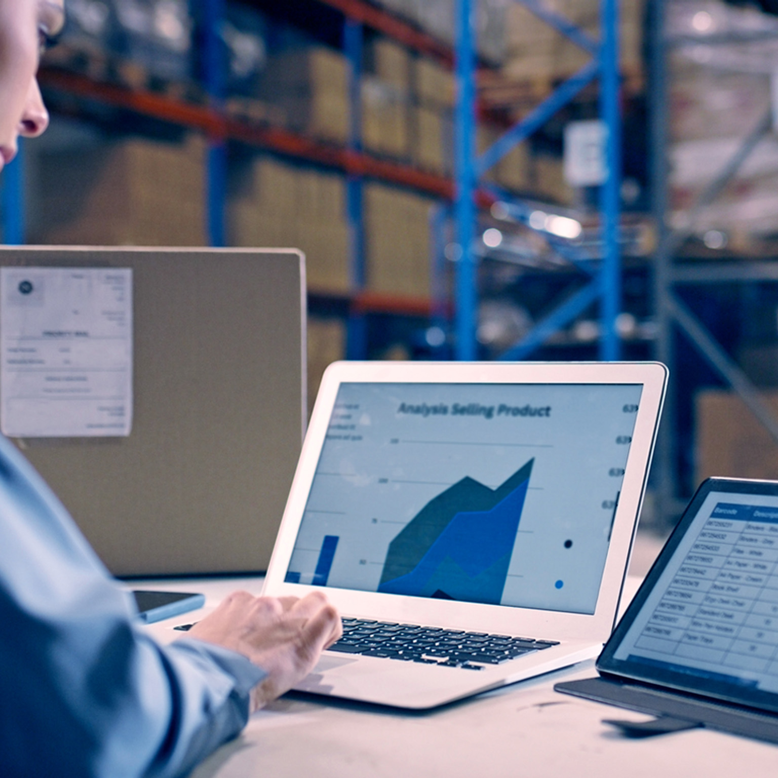 Woman working in a warehouse. Laptop screen is showing data analytics, e-commerce report and spreadsheet of sales.