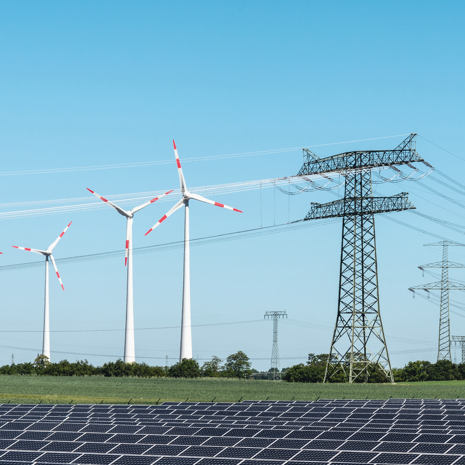 Grassy landscape with wind turbines, power lines, and solar panels.