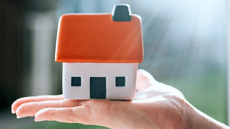 Model of a house with a red roof, held on a palm