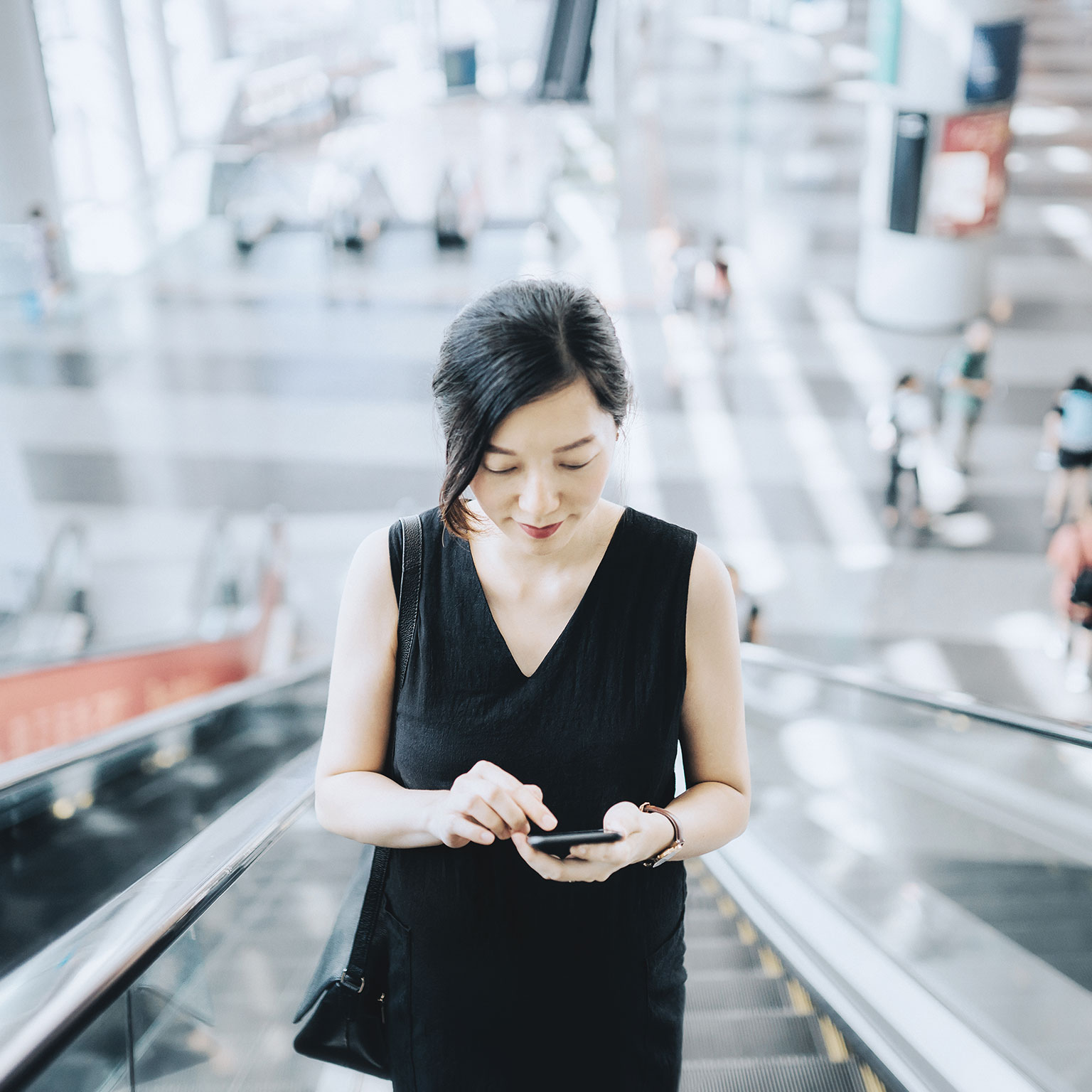 Young businesswoman reading emails on smartphone while riding on escalator