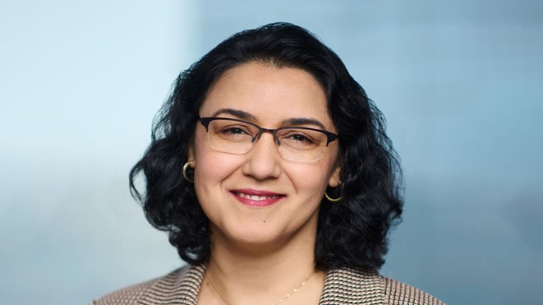 Portrait of a smiling Neeti Bhalla Johnson against a soft blue backdrop.