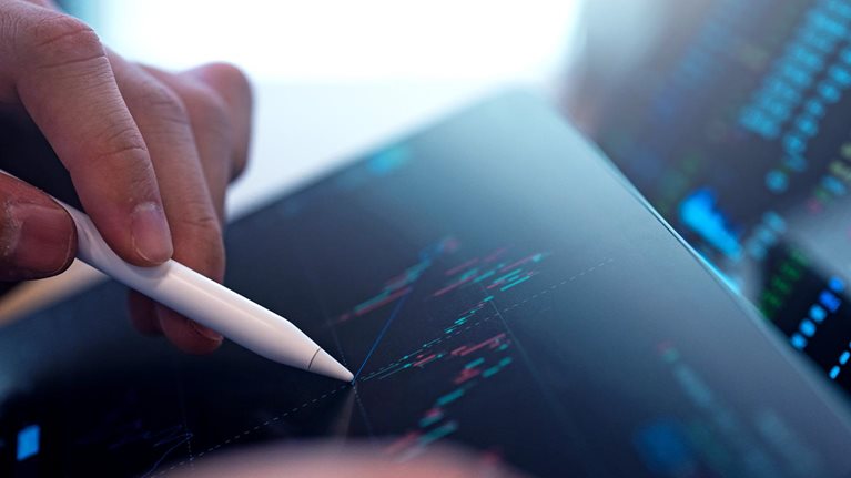 A business person tracking the technical movement of a stock chart on a computer screen.