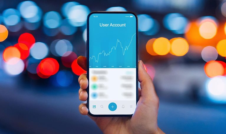 Woman's hand holding up smartphone against illuminated city street lights, using NFT investment wallet on smartphone in city, working with blockchain technologies.