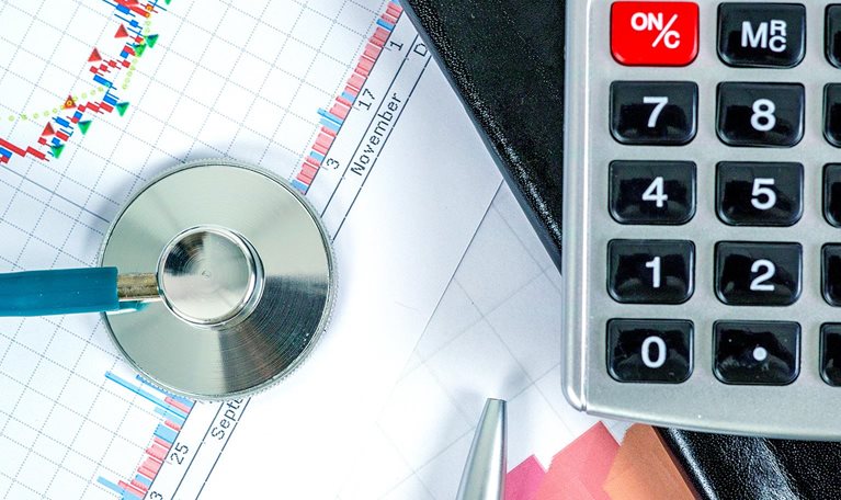 Top-down image of a stethoscope and a calculator on top of medical and healthcare business analysis reports.