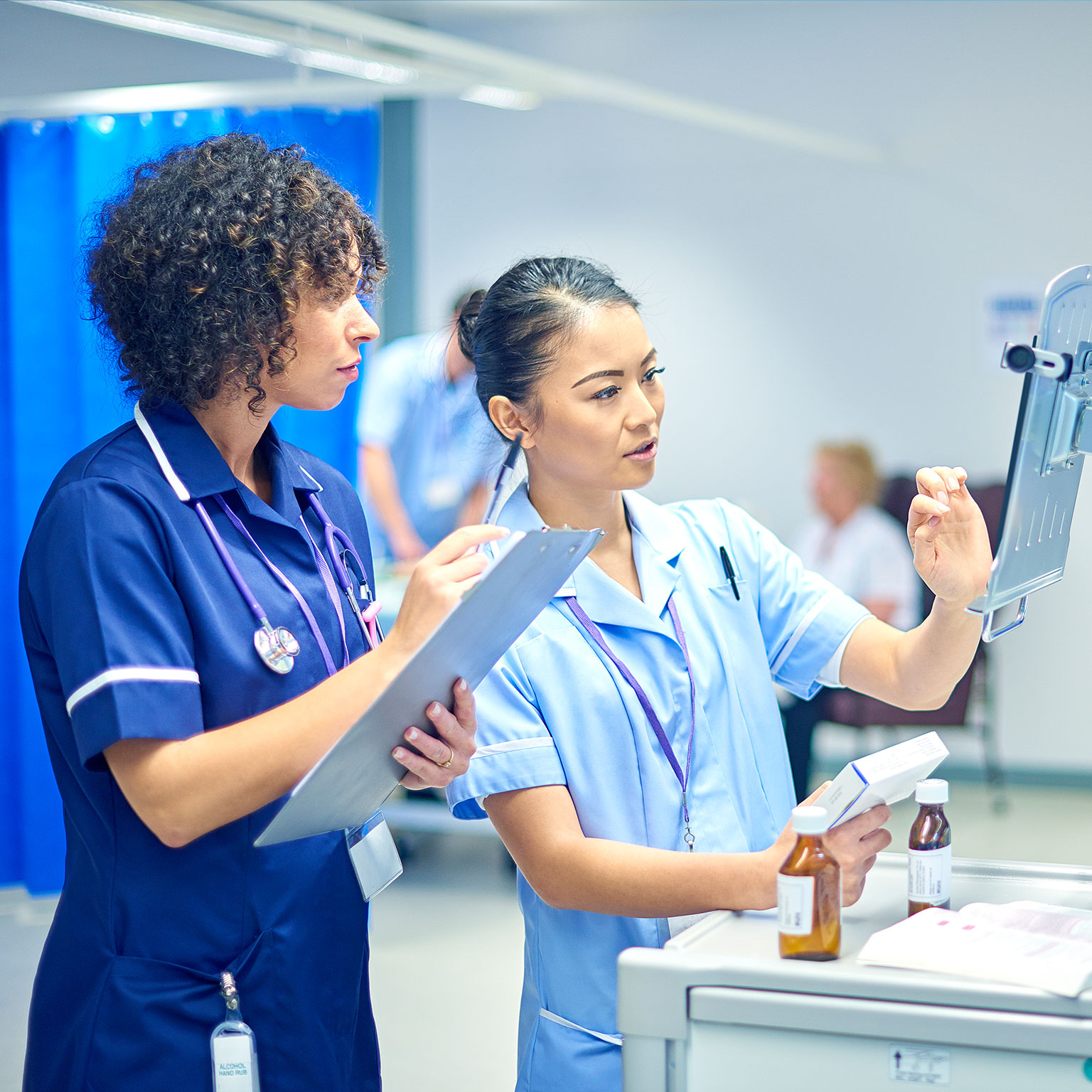 A young nurse checks the dosage on her digital tablet supervised by her staff nurse