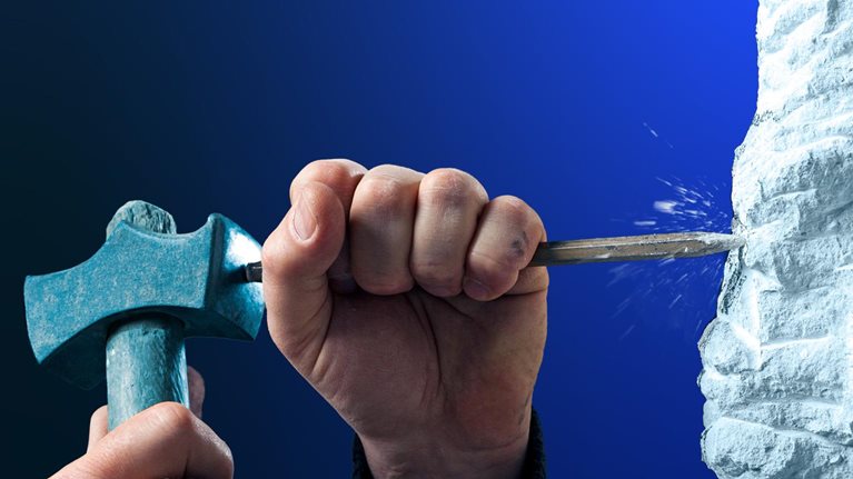 Two hands using a hammer and chisel to carve into a rough white stone surface. The close-up composition is set against a deep blue background.
