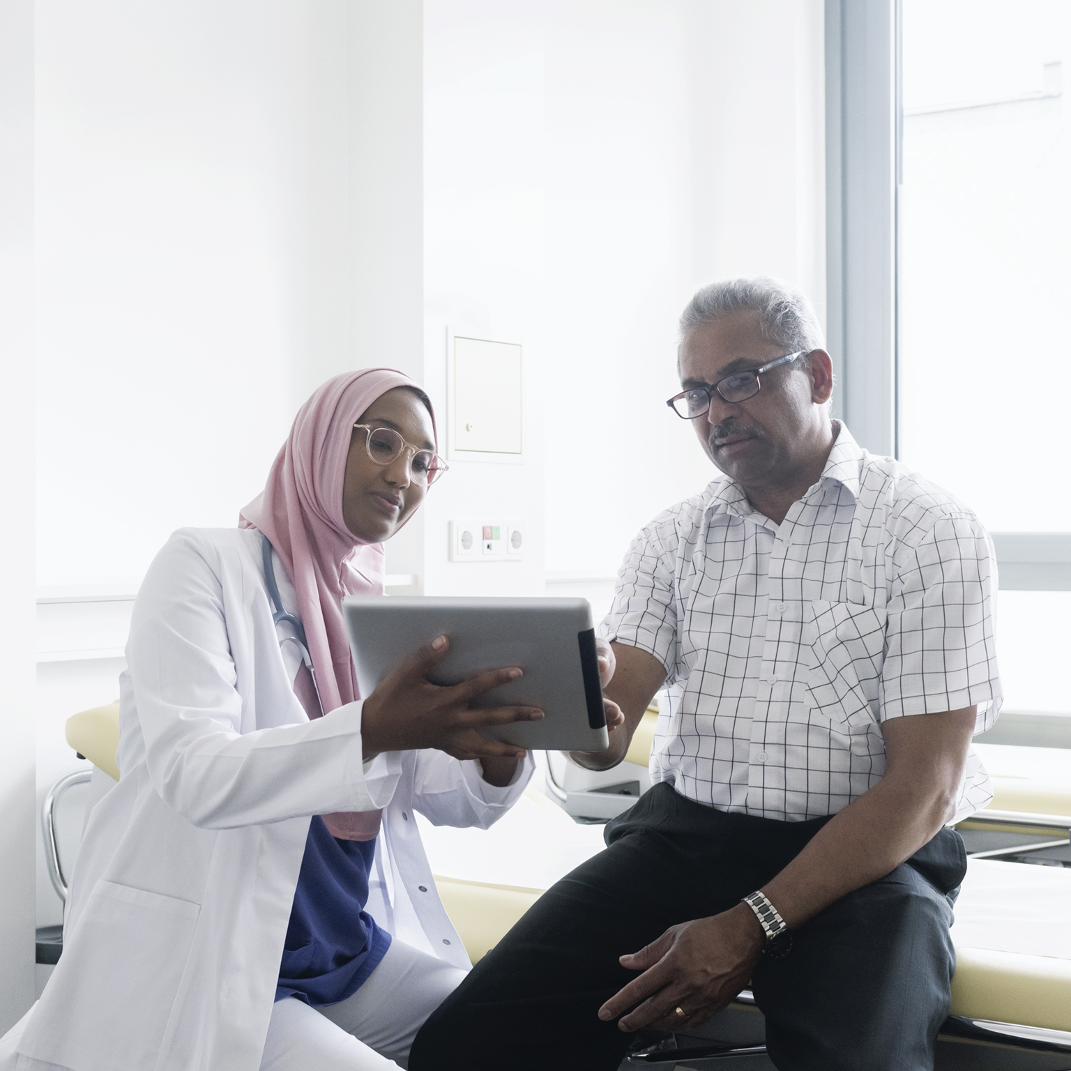 Female muslim doctor talking to senior patient using digital tablet