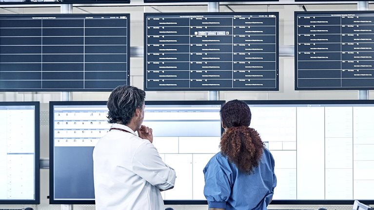 Medical professionals discussing the security system in front of an array of screens in a control room.