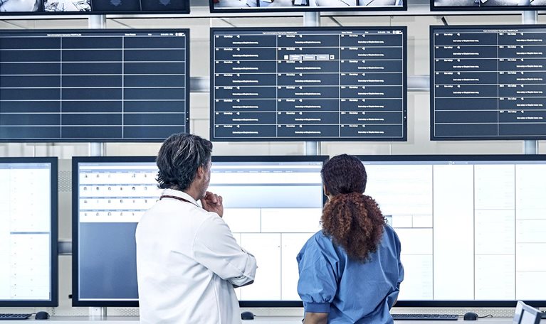 Medical professionals discussing the security system in front of an array of screens in a control room.