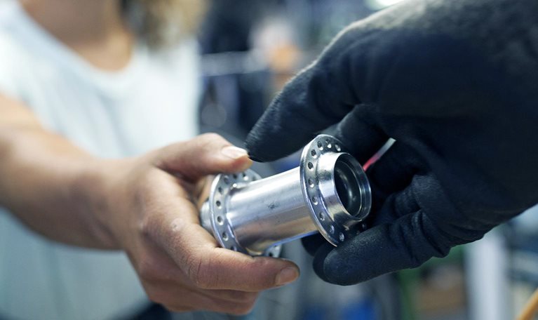 A close up of a technician handing her colleague a bike part while working together in a bicycle workshop