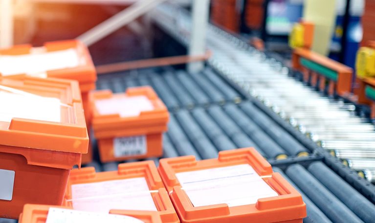 Warehouse conveyor belt with orange crates that are being packed with medicine