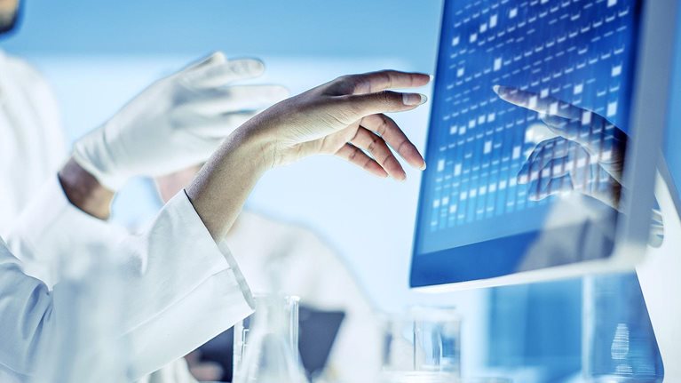 Close up image of scientists discussing and gesturing with their hands at data on a monitor.