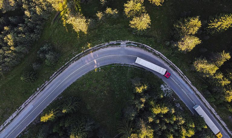 Drone point of view over two semi-trucks on a road curve in pine woodland.