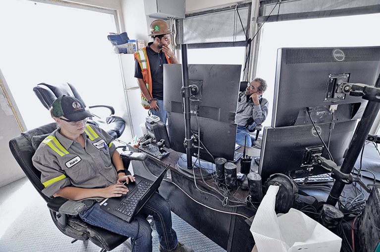 Metallurgist I Alaina Mallard, senior metallurgist Rahul Singh, and mill operator II Floyd (George) Mocaby discuss the expert system inside the ore crusher’s control room.