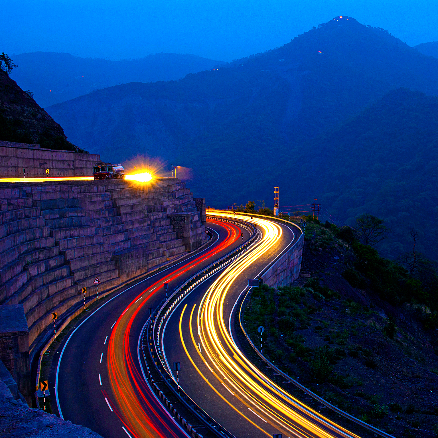 Red and white light trails on road at twilight in India mountain range 