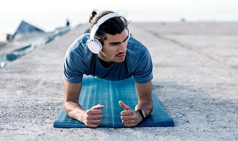 Young man wearing headphones planks on blue yoga mat