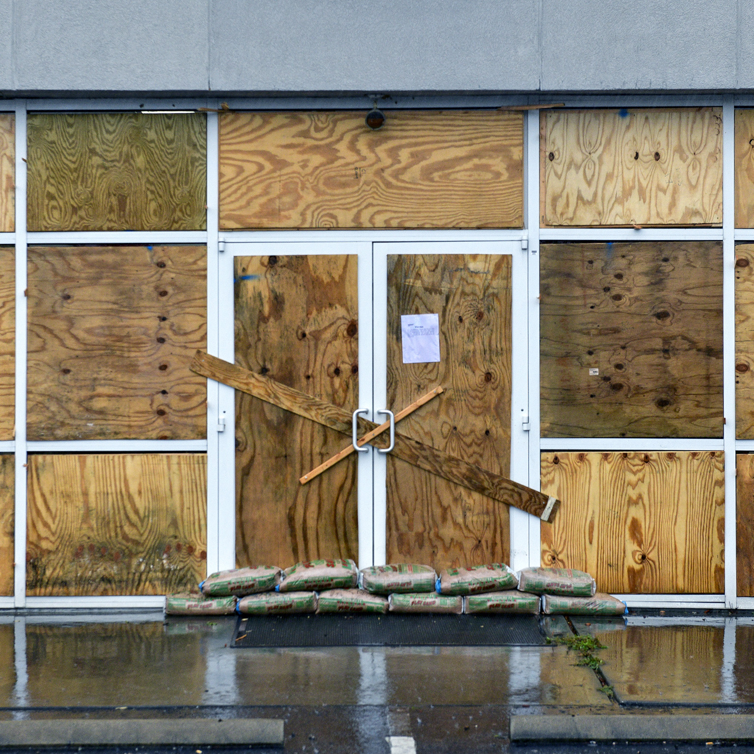 A shop with its large windows covered and sandbags placed in front of the entrance to protect if from an approaching Hurricane.