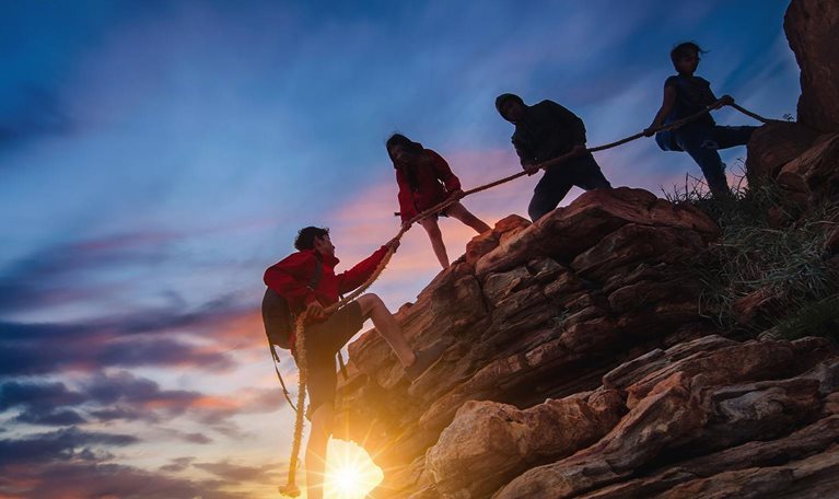 Hikers climbing up on the mountain at sunset ,teamwork and helping concept.
