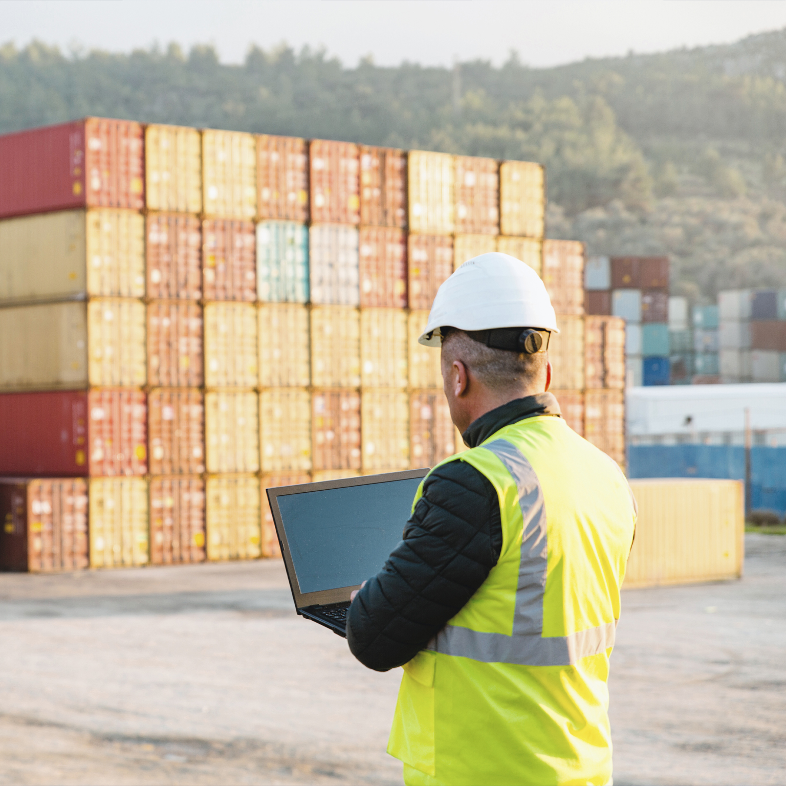 Engineer man with yellow crash helmet and worker west checking cargo freights in front of colorful cargo container stacks in shipping port