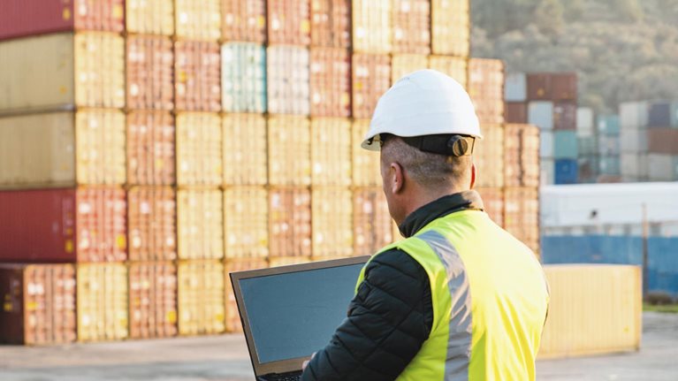 Engineer man with yellow crash helmet and worker west checking cargo freights in front of colorful cargo container stacks in shipping port