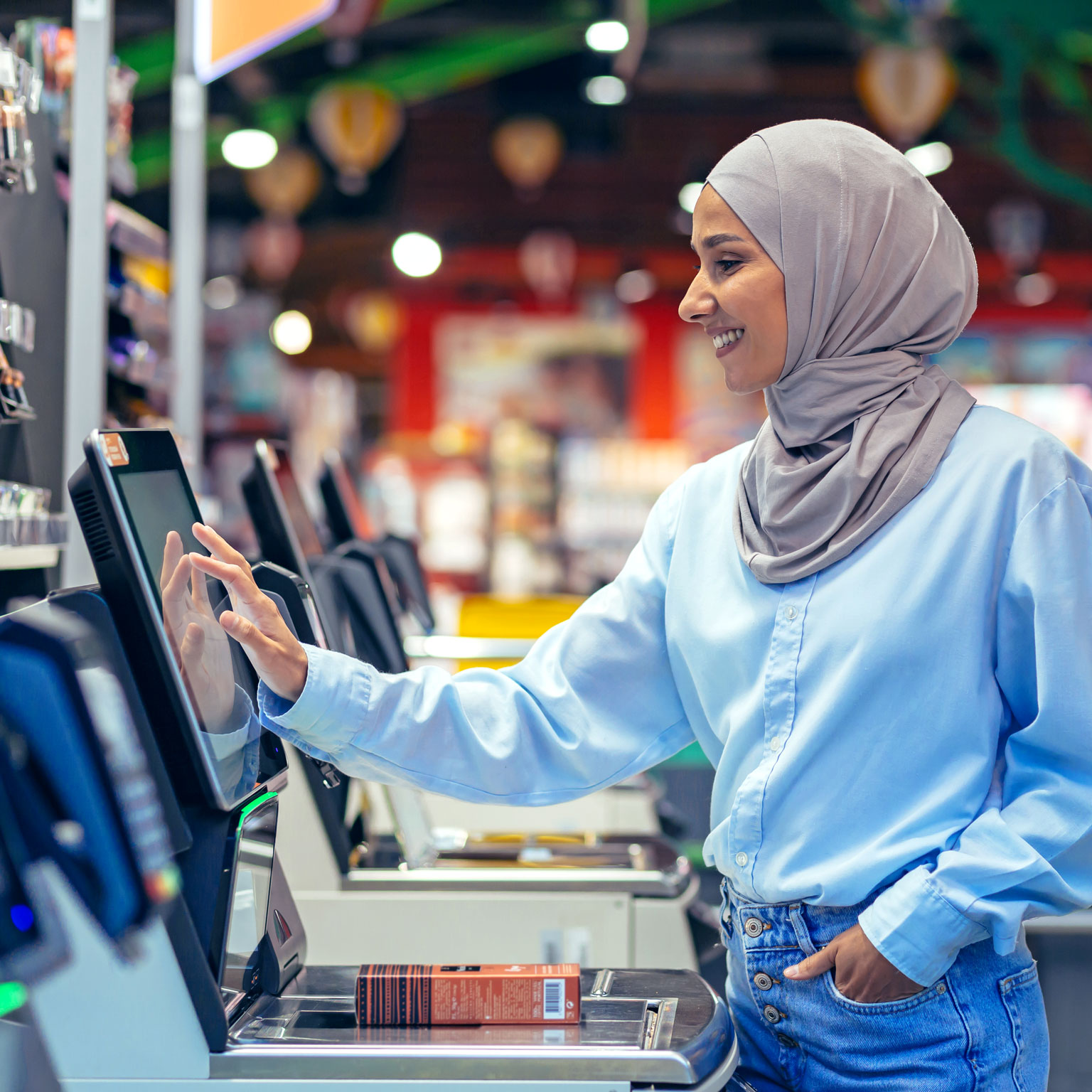 A woman buyer in a supermarket in a hijab pays for goods at a self-service checkout, convenient service for customers