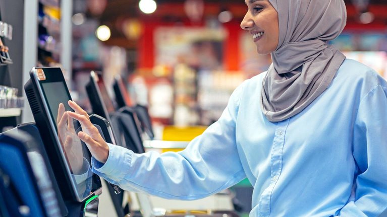 A woman buyer in a supermarket in a hijab pays for goods at a self-service checkout, convenient service for customers