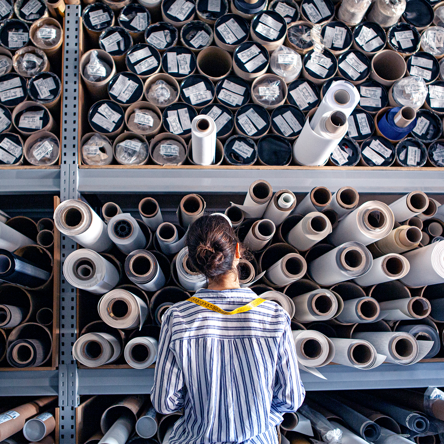Portrait of textile designer choosing fabric from stack of rolls inside sustainable workshop.