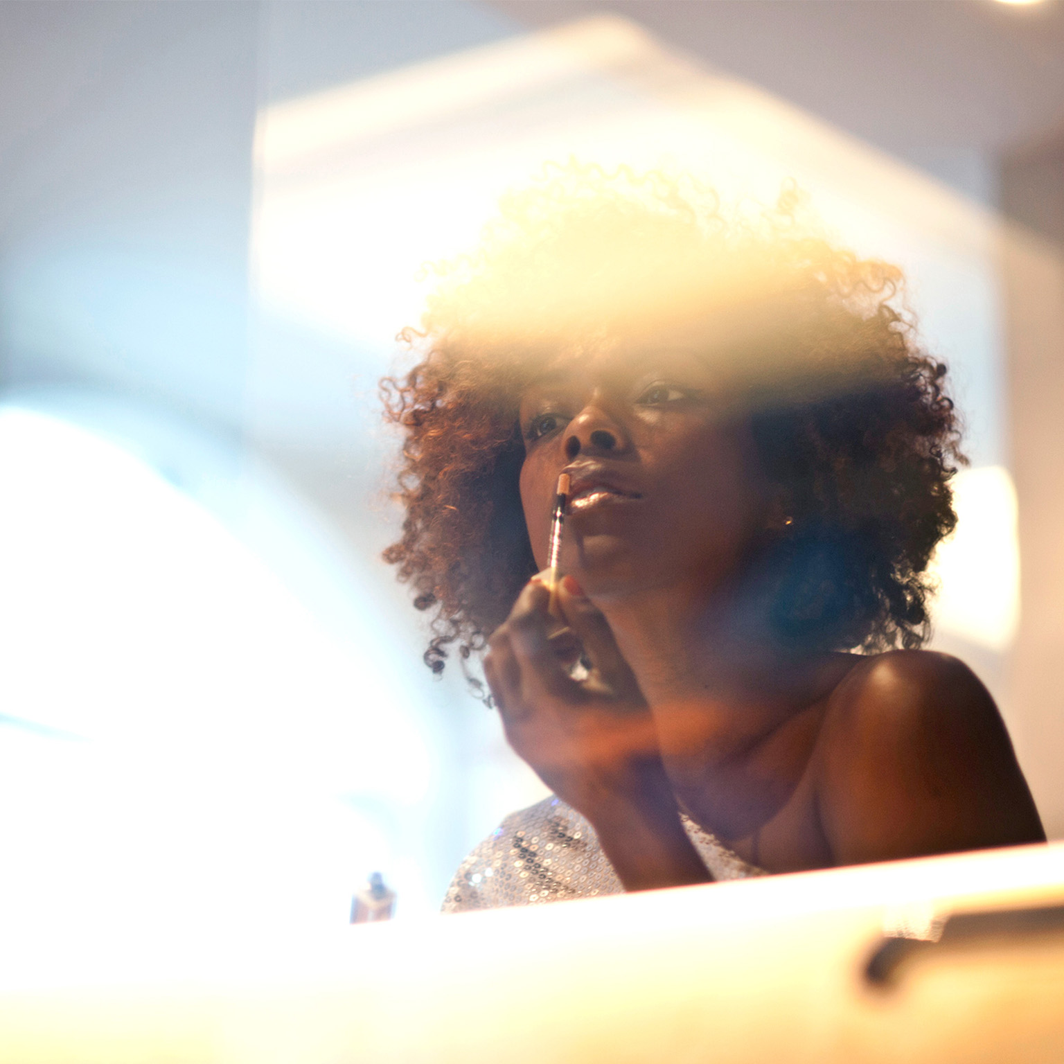 Black woman applying makeup in mirror