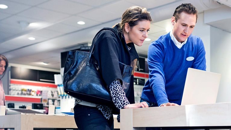 Salesman assisting female customer in buying laptop at store