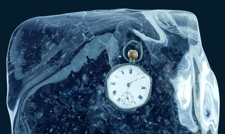 A pocket watch encased in a block of ice and set against a deep blue backdrop.