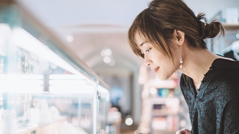 Young woman looking at jewelry through a glass display cabinet in a jewelry shop.