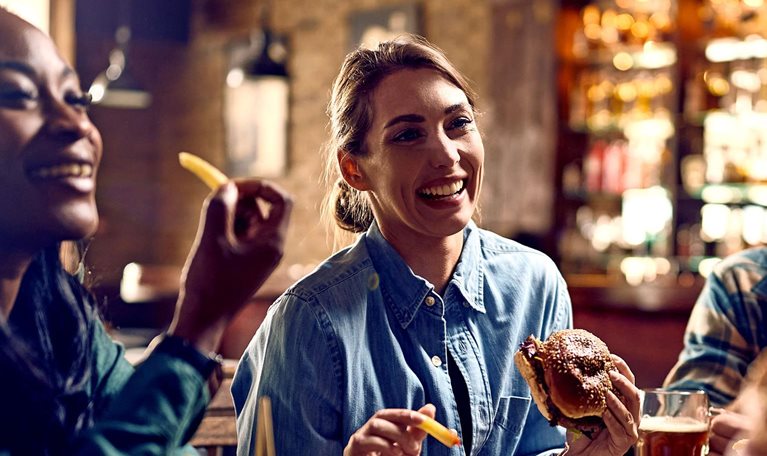 Multiracial group of happy friends eating burgers while drinking beer in a pub.