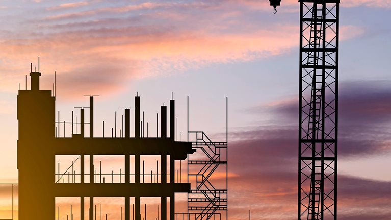 A skyline view of a construction site with cranes at sunset during construction of an apartment building