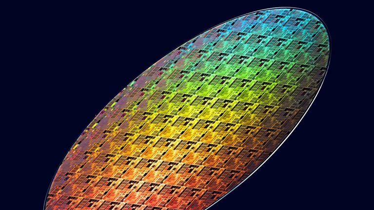 Colorful iridescent semiconductor wafer with intricate microchip patterns displayed against a dark background.