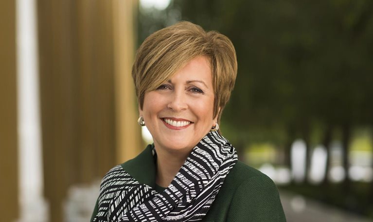 Portrait of a smiling Deborah Rutter in a forest green overcoat and scarf with black and white stripes.