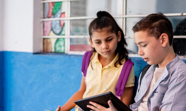 Child student friends talking and using digital tablet at school