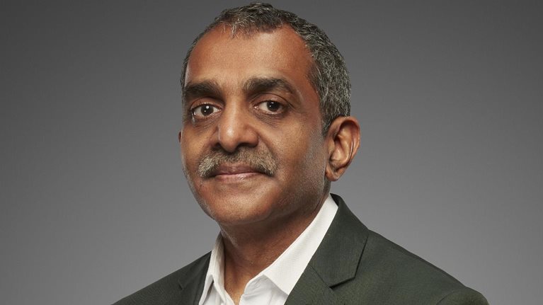 A portrait of Vijay Anand Guntur shows him wearing a gray suit jacket and a white button down shirt, exuding confidence with his gaze. He has well-groomed salt-and-pepper hair and a mustache.