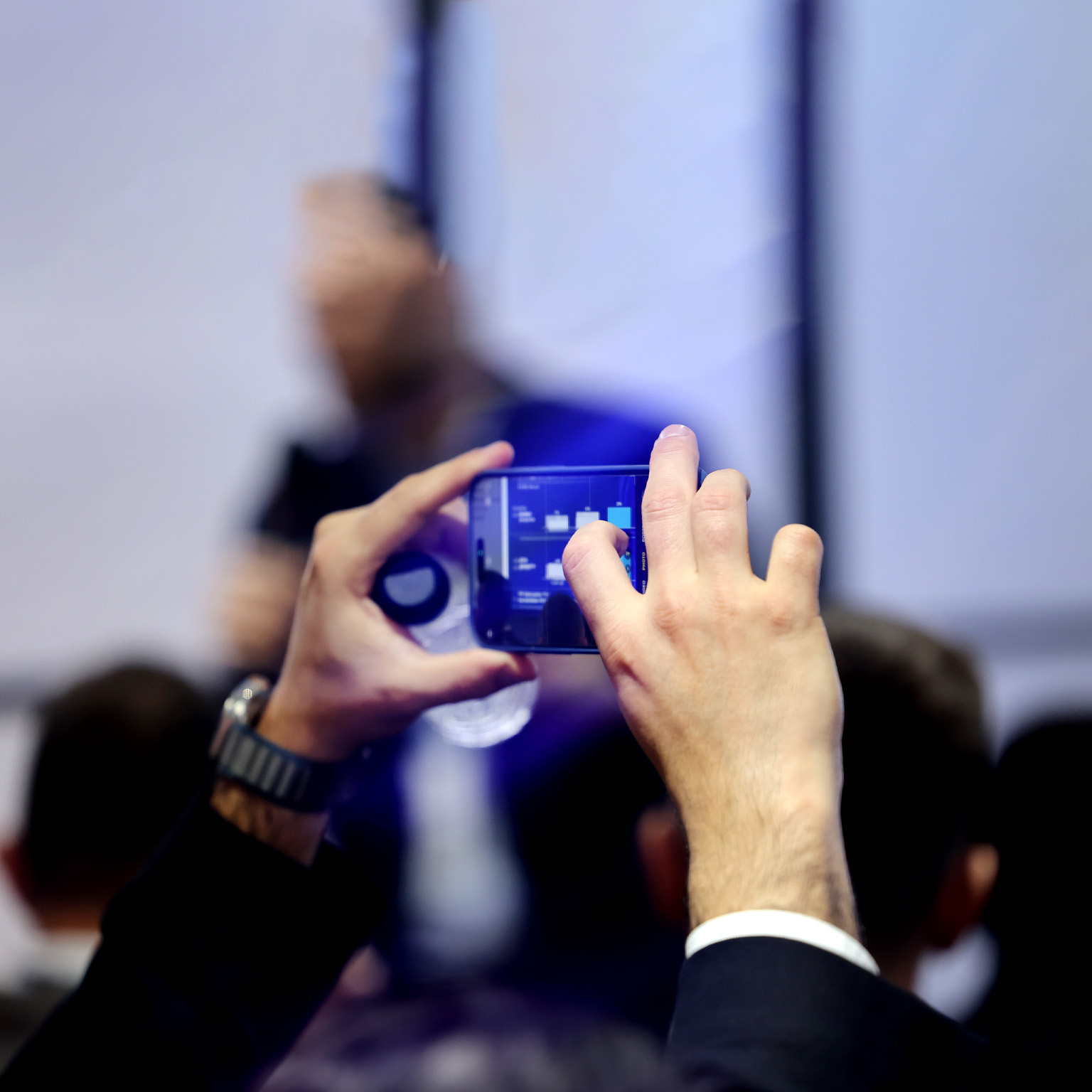 A close-up of hands holding a phone as they photograph a presentation of data visualizations at the Mobile World Congress.