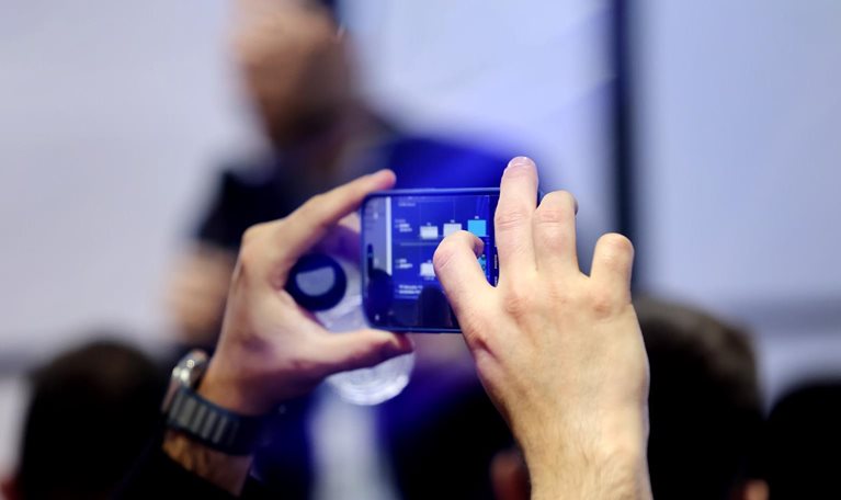 A close-up of hands holding a phone as they photograph a presentation of data visualizations at the Mobile World Congress.