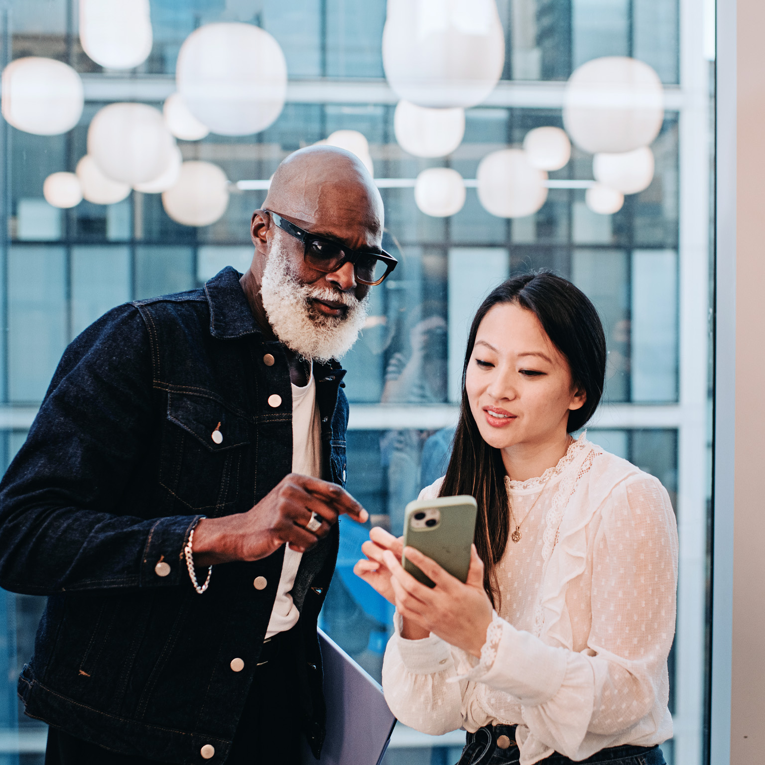 A woman shows a coworker something on her smart phone in an office setting.