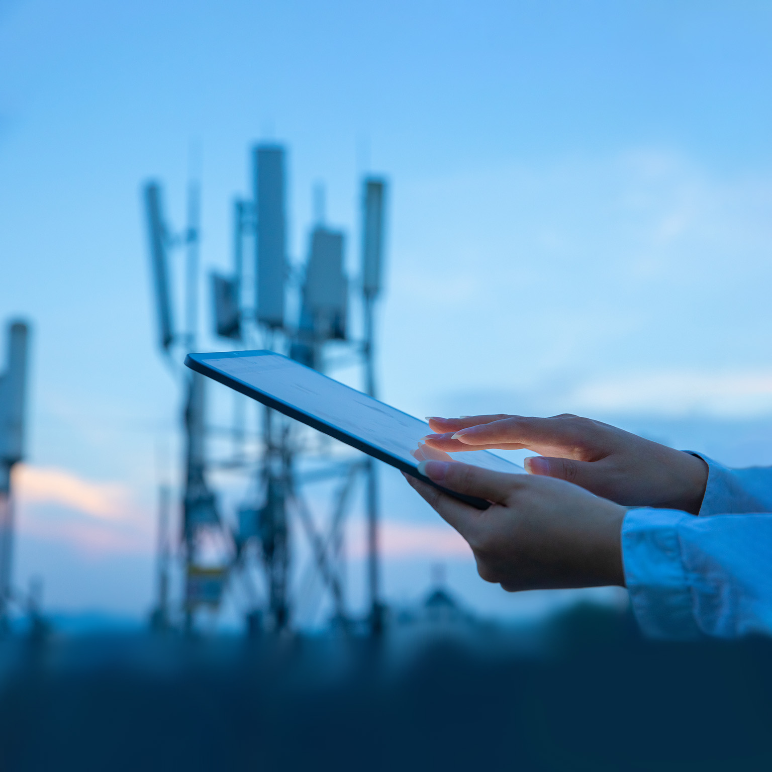 Close up of a hand touching a digital tablet near a 5G communications tower